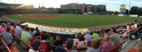 A panoramic view of a baseball game with a crowd in the foreground and players on the field in the background.