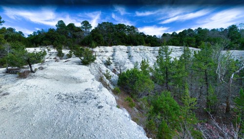 A rocky cliffside with green trees and a blue sky, showcasing a natural landscape with layered white rock formations.
