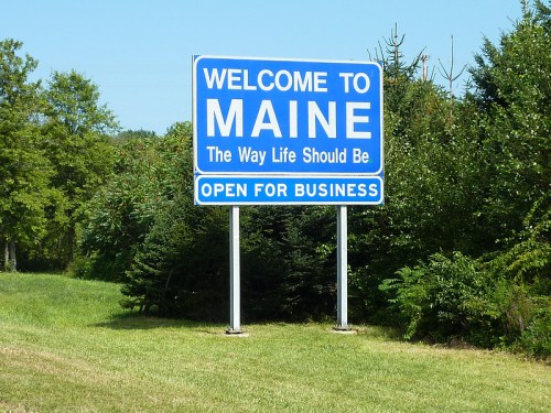 Welcome to Maine sign with the slogan "The Way Life Should Be" and "Open for Business" against a clear blue sky.