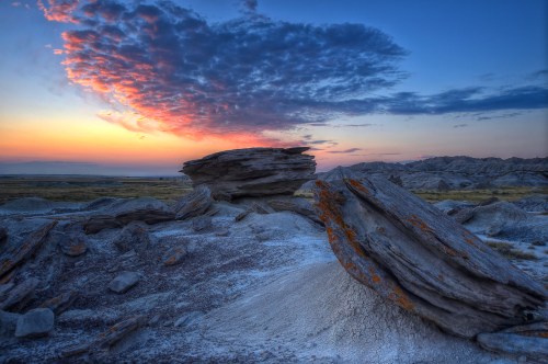 A stunning sunset over rocky terrain, with vibrant clouds and layered rock formations in a serene landscape.