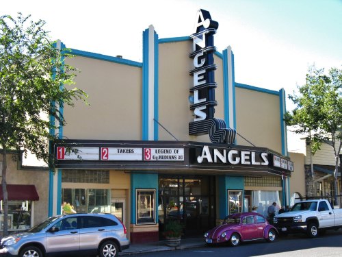 Historic theater building with "Angels" sign, marquee displaying movie titles, and vintage cars parked outside.