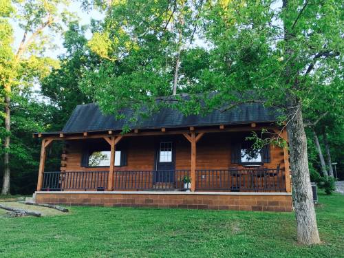 A cozy wooden cabin with a porch, surrounded by lush green trees and grass.
