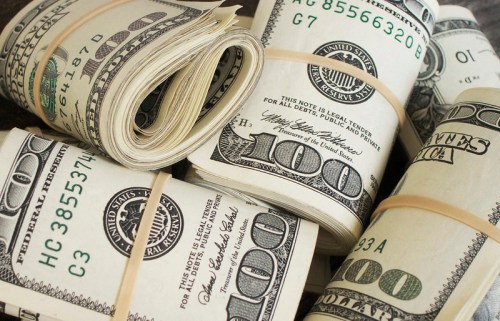 Stacks of rolled hundred-dollar bills secured with rubber bands, arranged on a flat surface.