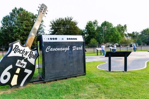 A large guitar and amplifier display at Cavenaugh Park, with people enjoying the outdoor space in the background.
