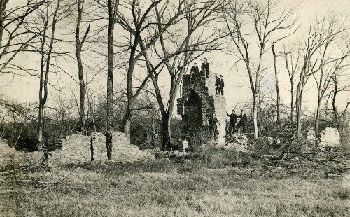 Black and white photo of a stone ruin surrounded by bare trees, with people standing on and around the structure.