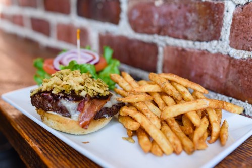 A plate with a burger topped with crispy onions, bacon, and cheese, served with a side of golden French fries and fresh veggies.