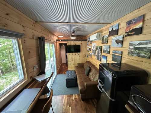 Cozy interior of a tiny cabin featuring a sofa, dining area, and wall art, surrounded by nature.