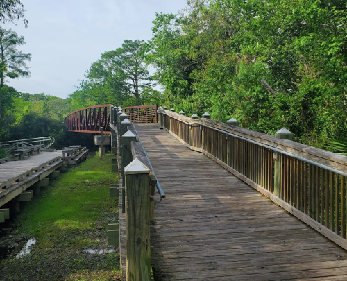 A wooden walkway leads through lush greenery, with a curved bridge visible in the background.