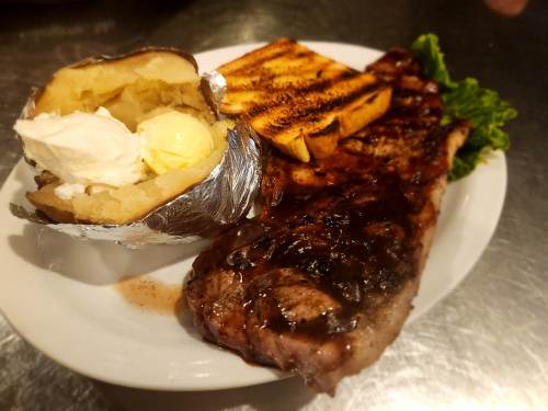 A plate featuring a grilled steak, baked potato with butter, toasted bread, and a side of lettuce.