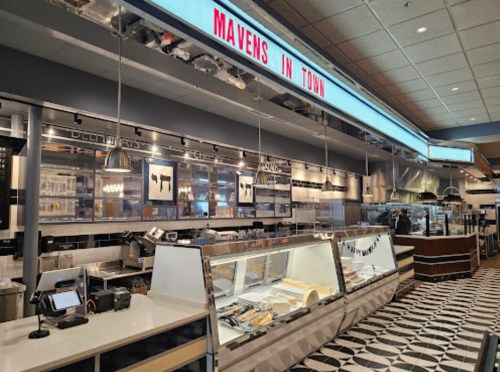 Interior of a modern deli named "Mavens in Town," featuring display cases and a stylish black-and-white tiled floor.