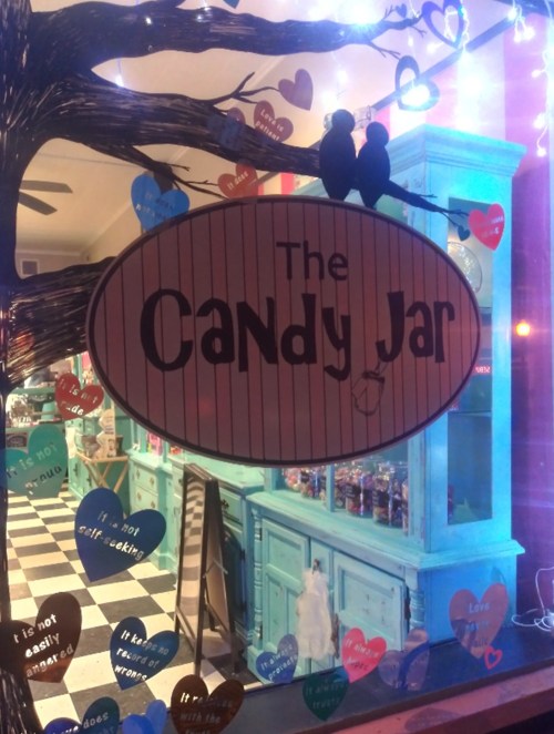 A window display featuring "The Candy Jar" sign with colorful heart decorations and a whimsical tree design.