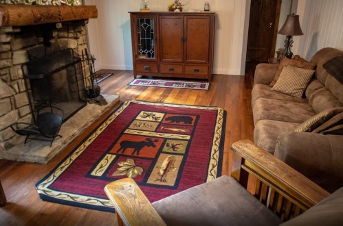 Cozy living room with a stone fireplace, wooden furniture, and a patterned rug featuring wildlife and nature motifs.