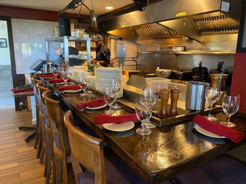 A restaurant kitchen with a long table set for dining, featuring plates, glasses, and a chef in the background.