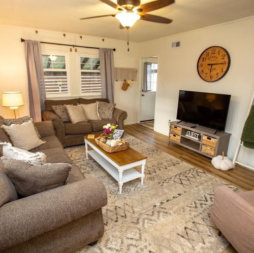 Cozy living room with a sofa, armchair, coffee table, TV, and decorative elements, featuring warm lighting and a rug.