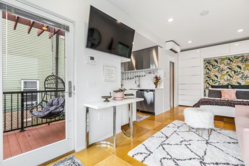Cozy studio apartment with modern decor, a small kitchen, and a balcony featuring a hanging chair.