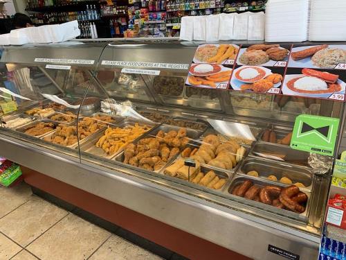 A display case filled with various fried foods, including chicken, sausages, and pastries, in a convenience store.