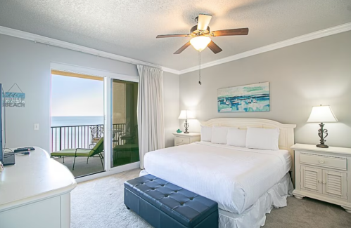 Bright bedroom with a king-size bed, two lamps, a balcony view, and coastal decor.