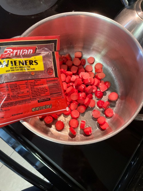 A pot on the stove with chopped hot dogs and an open package of hot dogs beside it.