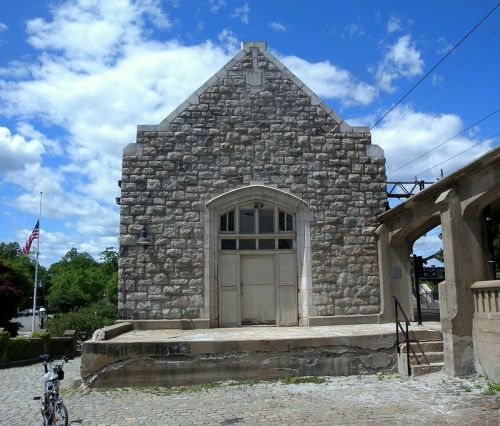 Stone building with a large arched entrance, set against a blue sky with clouds, and a bicycle parked nearby.