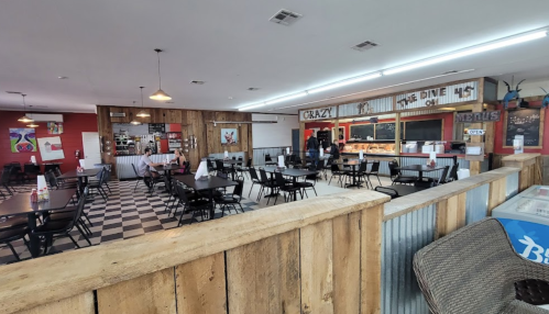 Interior of a casual restaurant with black and white checkered floors, wooden accents, and empty tables.