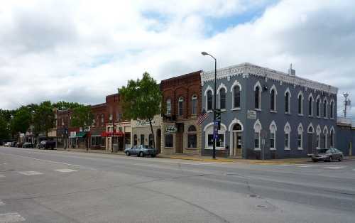 A quaint street scene featuring historic brick buildings, shops, and trees under a cloudy sky.