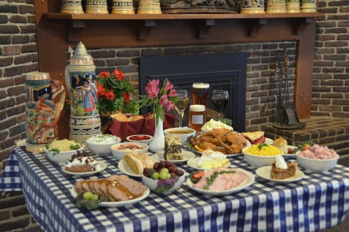 A festive table set with various dishes, including meats, salads, and desserts, in a cozy, rustic setting.