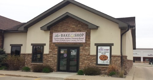 A bakery storefront with a stone facade, featuring a sign for "Aunt's Bake Shop" and various baked goods listed.
