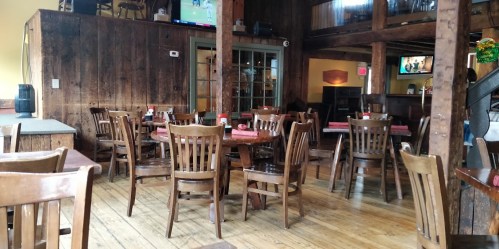 Cozy restaurant interior with wooden tables and chairs, featuring a rustic design and a TV in the background.