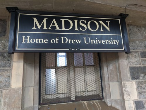 Sign reading "MADISON Home of Drew University" above a window with a metal grate.