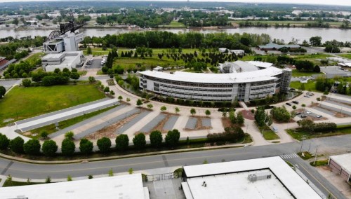 Aerial view of a modern building surrounded by green spaces and a river in the background.