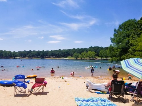 A sunny beach scene with people swimming, lounging on chairs, and enjoying the water under a clear blue sky.