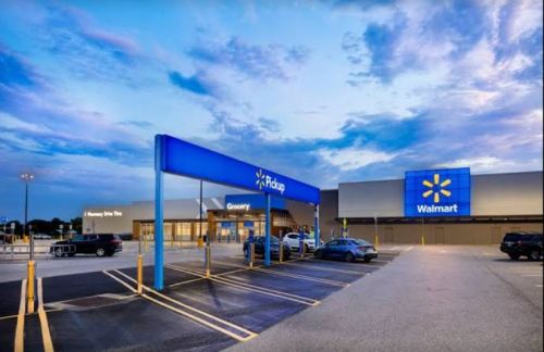 Walmart storefront with a grocery pickup area, under a cloudy sky, featuring parked cars in the lot.