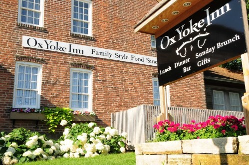 Sign for Ox Yoke Inn with flowers in front, showcasing family-style food, lunch, dinner, bar, and Sunday brunch.