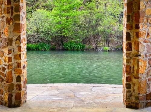 View of a serene green river framed by stone pillars and lush greenery in the background.