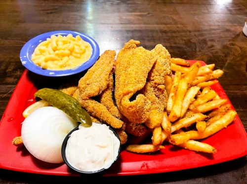 A red plate with fried fish, French fries, macaroni and cheese, onion, pickle, and dipping sauce.