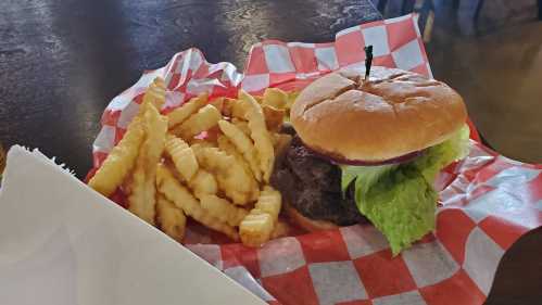 A juicy burger with lettuce and onion, served with crinkle-cut fries on a red and white checkered paper.