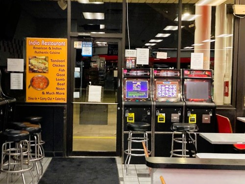 Interior of an India restaurant featuring slot machines, tables, and a menu sign highlighting various dishes.