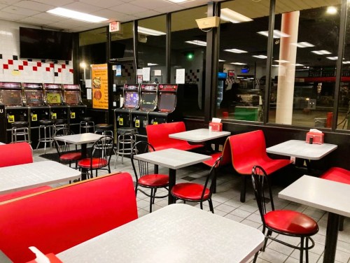 Empty diner with red chairs and tables, featuring slot machines in the background and large windows showing a night view.