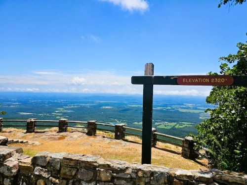 A scenic view from a mountain overlook, featuring a sign indicating an elevation of 2320 feet and lush green valleys below.