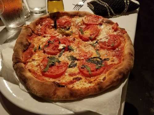 A freshly baked pizza topped with tomatoes, basil, and melted cheese, served on a white plate.