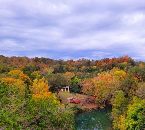A scenic view of a river surrounded by vibrant autumn foliage and a grassy area with a small gathering space.