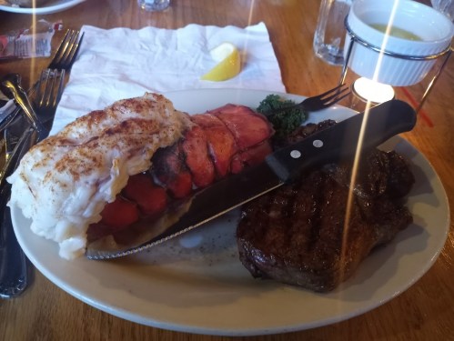 A plate featuring a lobster tail, steak, and a knife, garnished with a lemon wedge and parsley.