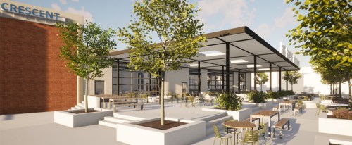 Modern outdoor space with trees, tables, and a covered seating area, adjacent to a brick building labeled "CRESCENT."