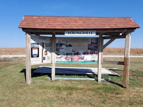 Information kiosk about Youngville, featuring historical displays and a wooden shelter against a clear blue sky.