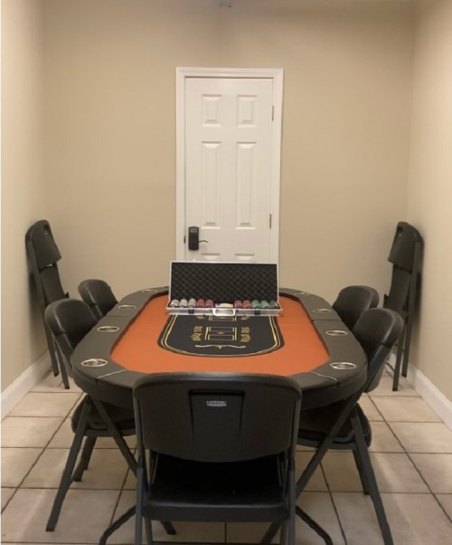 A poker table with chairs arranged around it, featuring a set of poker chips in a case on the table.
