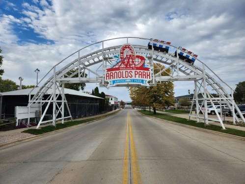 Entrance archway to Arnolds Park Amusement Park, with a cloudy sky and a wide road leading into the park.