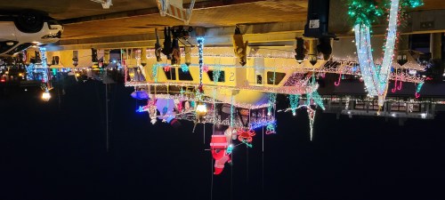 A brightly lit boat decorated for Christmas, with people walking nearby and festive lights illuminating the scene.