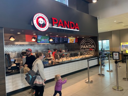 A family approaches the counter of a Panda Express restaurant, with staff preparing food in the background.