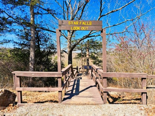 A wooden lookout platform with a sign reading "Star Falls Look Out," surrounded by trees and a clear blue sky.