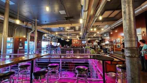 A vibrant bar interior with seating, dim lighting, and a lively atmosphere, featuring people socializing and enjoying drinks.